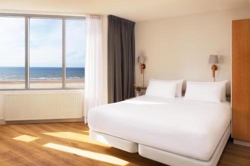 a bedroom with a large white bed with a view of the ocean at NH Zandvoort Hotel in Zandvoort