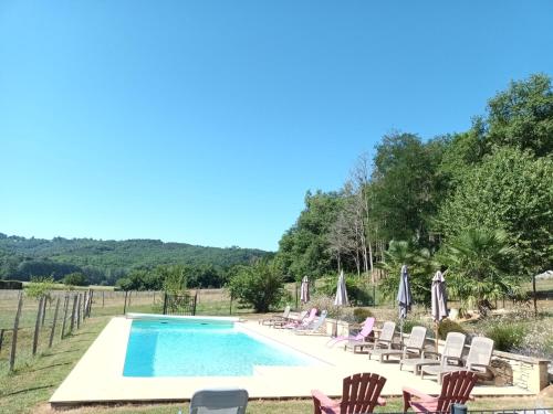 une piscine avec des chaises et des personnes assises autour de celle-ci dans l'établissement Le Séchoir des acacias, Gîte La Noyeraie, à Saint-Léon-sur-Vézère