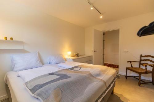 a bedroom with a large bed and a chair at Zeesamen 5 min from beach in Cadzand