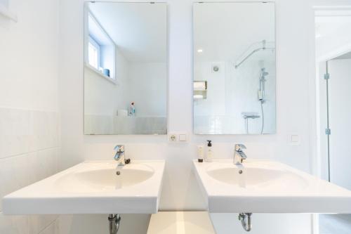 two sinks in a white bathroom with mirrors at Zeesamen 5 min from beach in Cadzand