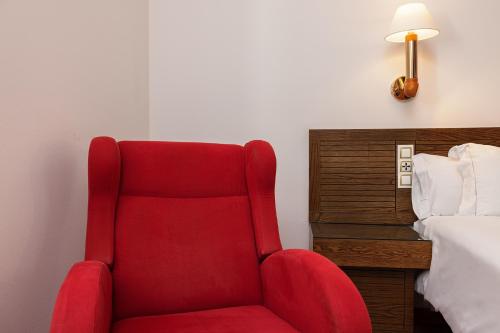 a red chair sitting in a room next to a bed at Senator Cádiz in Cádiz