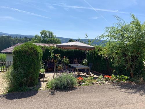 a patio with a table and an umbrella and flowers at Chez Eli in Le Sentier
