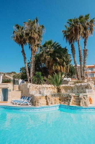 a swimming pool with palm trees and lounge chairs at Xemxija Bay Hotel in St Paul's Bay