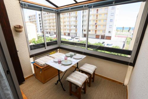 une table et des chaises dans une pièce avec une grande fenêtre dans l'établissement Saint-Cyprien charmant appartement vue mer, à Saint Cyprien Plage