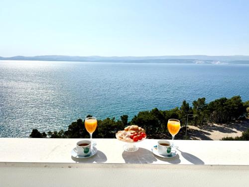 two glasses of orange juice and a bowl of fruit and a bowl of food at Apartman Mali Raj in Lokva Rogoznica