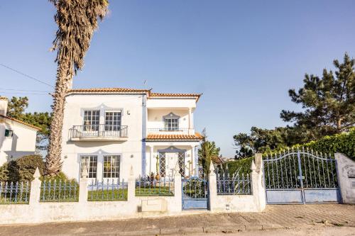 a white house with a fence and a palm tree at Santa Cruz Surf House by Stoke Travel in A dos Cunhados