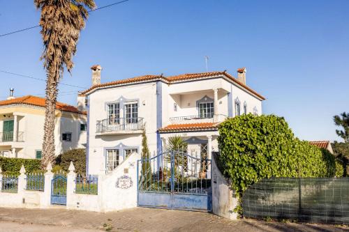 a white house with a fence and a palm tree at Santa Cruz Surf House by Stoke Travel in A dos Cunhados
