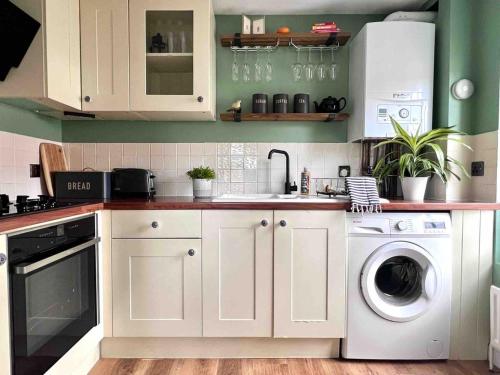 a kitchen with white cabinets and a washer and dryer at Cosy Georgian Cottage - Parking - Central Frome in Frome