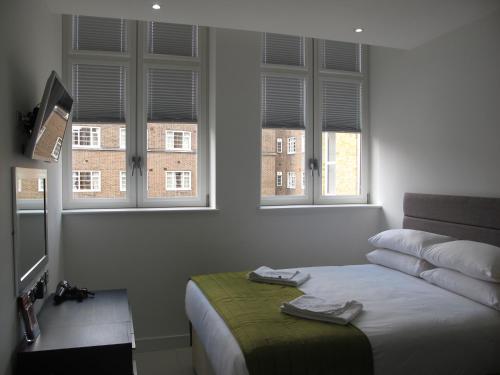 a bedroom with a bed and two windows at BLOOMSBURY APARTMENTS in London