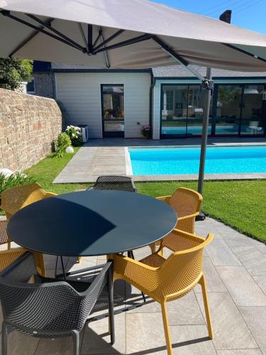 - une table et des chaises sous un parasol à côté de la piscine dans l'établissement Jolie Maison avec piscine, proche Mt St Michel, à Avranches
