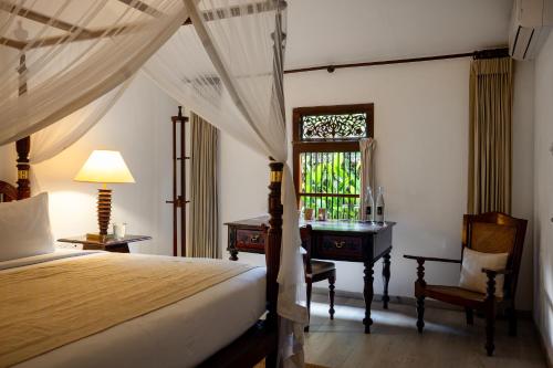 a bedroom with a bed and a desk and a window at Nyne Hotels Rock Villa - Bentota in Bentota