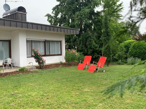 three red chairs sitting in a yard next to a house at Bodensee Bungalow in Immenstaad am Bodensee