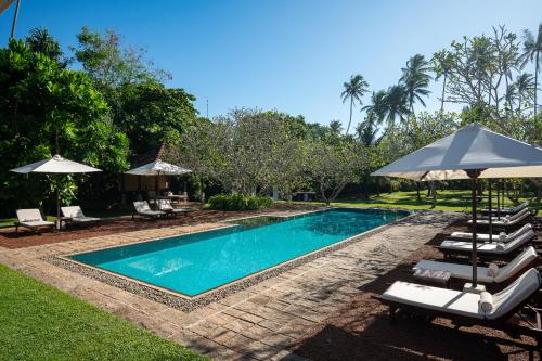 a swimming pool with chairs and umbrellas next to a resort at Nyne Hotels Rock Villa - Bentota in Bentota