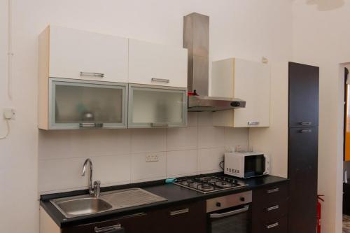 a kitchen with white cabinets and a sink and a microwave at House next to sea, grand & unique Maltese style in St Paul's Bay