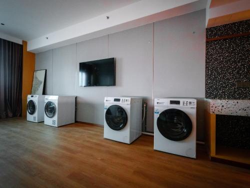 a laundry room with three washing machines and a tv at Shō Hotel BreakX in Jelutong