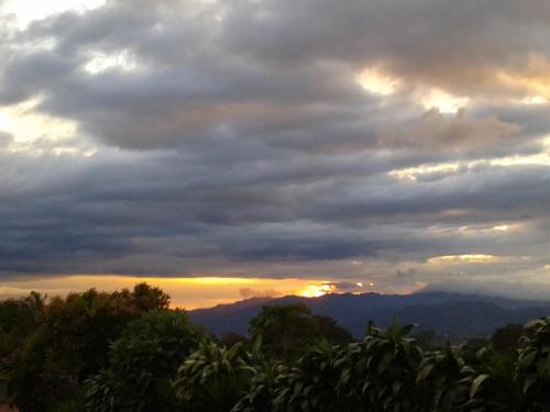 a cloudy sky with the sun setting in the mountains at Lagunillas Del Poas in Poasito