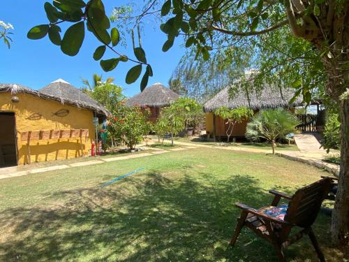 a yard with a chair and a building with thatched roofs at Caju Bangalôs in Ponta do Anel