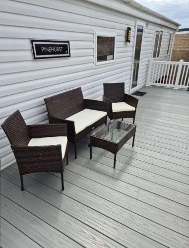 a deck with three chairs and a table and a sign at Camber Sands Holiday Park in Camber