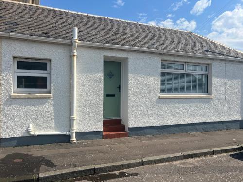 a white house with a green door on a street at Links Cottage, Prestwick in Prestwick