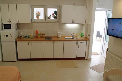 a kitchen with white cabinets and a sink and a tv at Adria Apartments in Podgora