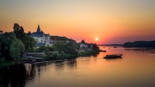 a sunset over a river with a castle and a boat at La maison familiale des bords de Loire in Turquant