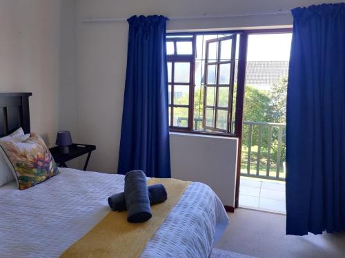 a bedroom with a bed with blue curtains and a large window at Aletheia Abode in Port Alfred