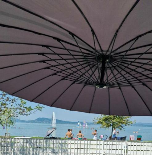 a purple umbrella on a beach with people and a sailboat at Sunset Beach House in Fonyód
