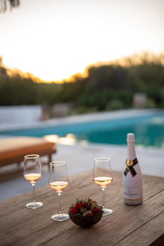three glasses of wine and a bowl of strawberries on a table at Villa Zina Sunset View St Lazaros 7 plus 1 Bedroom in Psarou