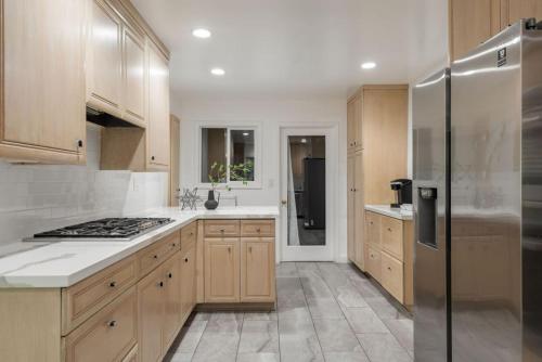a kitchen with wooden cabinets and a stainless steel refrigerator at Overlooking Luxury - Pool Heat - Spa - Games in Pico Rivera