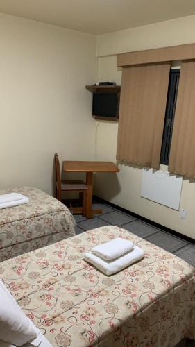 a room with two beds and a table and a desk at Goldmen Business Criciúma in Criciúma