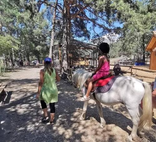 deux filles chevauchant un cheval blanc à côté d'une femme dans l'établissement La cabane enchantée, Logement Insolite à La Ferme, à Le Vernet