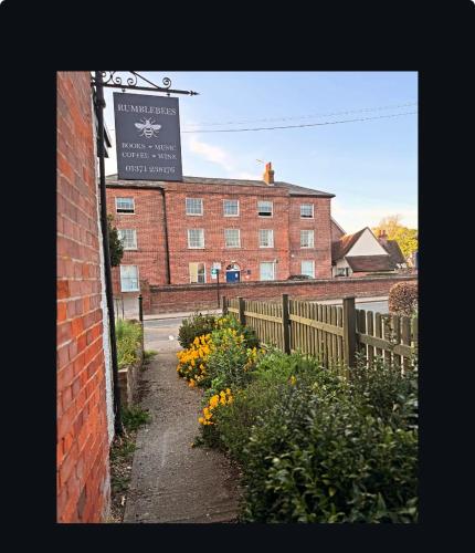 a brick building with a sign on it and flowers at Upstairs at Rumblebees in Felsted Station