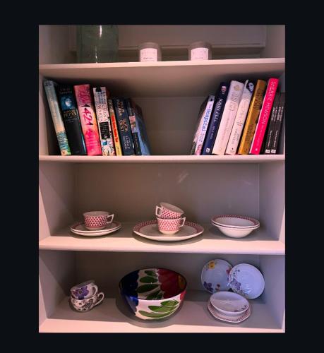 a book shelf filled with books and plates and bowls at Upstairs at Rumblebees in Felsted Station