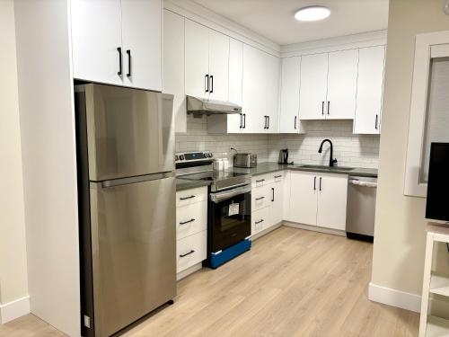 a kitchen with white cabinets and a stainless steel refrigerator at Sunny White Rock 2BR, Steps to Sand, Brand New Stay in White Rock