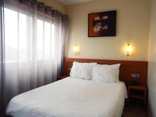 a bedroom with a bed with white sheets and a window at Hotel São Francisco in Leiria