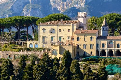 ein großes Haus auf einem Hügel mit Bäumen und Bergen in der Unterkunft Hotel Villa Cimbrone in Ravello