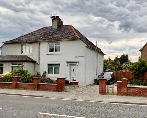 a white house with a brick fence in front of it at Ashley Holiday Home, Close To City Centre With Free Parking in Dalneigh
