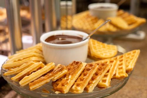 a plate of waffles and a cup of chocolate sauce at Del Rey Quality Hotel in Foz do Iguaçu