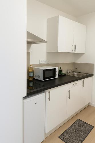 une cuisine avec des placards blancs et un four micro-ondes sur un comptoir dans l'établissement Golden House - Gare & Centre, à Troyes