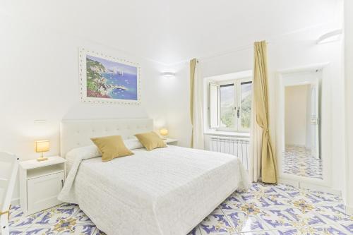 a white bedroom with a bed and a window at Palazzo Trara - Holiday Rooms in Scala
