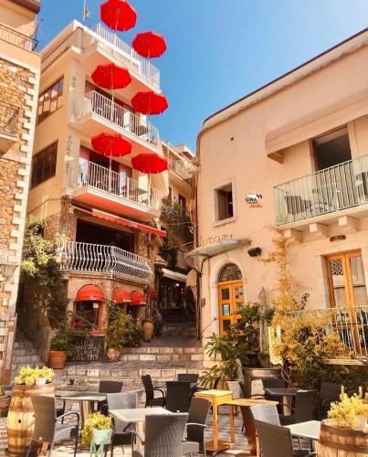 a patio with tables and red umbrellas in front of a building at Tyche House Castelmola in Castelmola