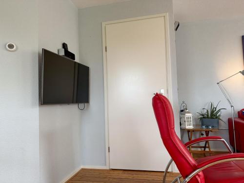 a room with a red chair and a television on a wall at Aquamarijn in Stavoren