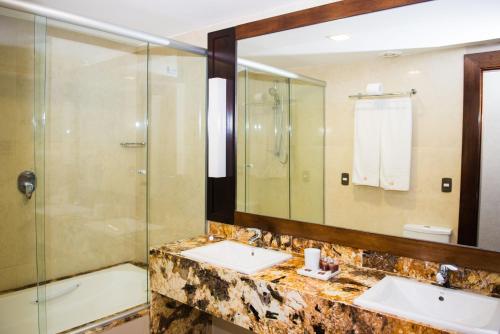a bathroom with two sinks and a shower and a mirror at Royal Atlântica Macaé Hotel in Macaé
