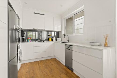 a white kitchen with white cabinets and a wooden floor at Coastal 2-Bed Apartment Steps from Manly Beach in Sydney