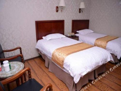 two beds in a hotel room with a table and chairs at GreenTree Inn Harbin Central Avenue in Harbin