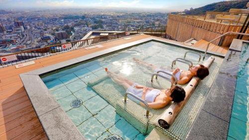 two women swimming in a swimming pool on top of a building at Ooedo Onsen Monogatari Minoh Kanko Hotel in Minoo
