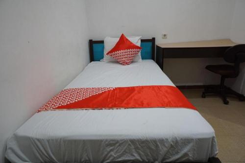 a bed with a red and white blanket and a desk at OYO 92863 Hotel Blessing in Surabaya