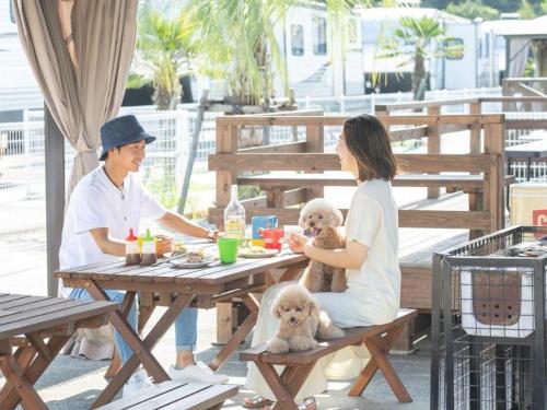 un homme et une femme assis à une table de pique-nique avec un chien dans l'établissement THE TRAILERHOUSE VILLAGE AMAKUSA MARINA, à Nobotate