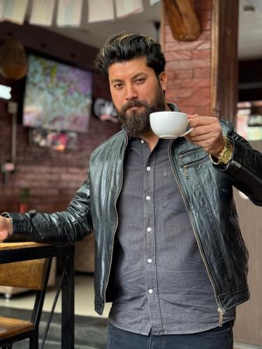 a man in a leather jacket holding a cup of coffee at Butterfly Lodge in Pokhara