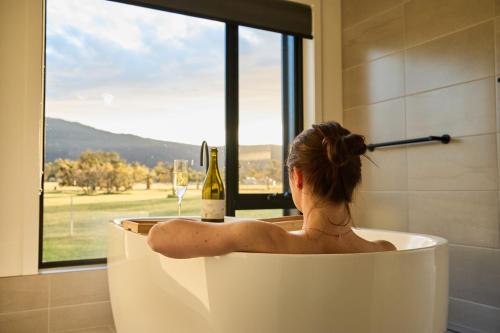 a woman sitting in a bath tub with a bottle of wine at Pomonal Estate Villas in Pomonal